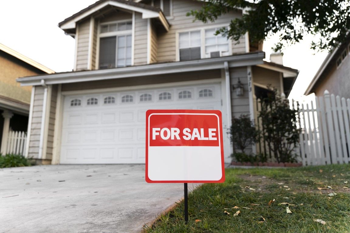 A ‘For Sale’ sign stands on the front lawn of a house, indicating the property is on the market.