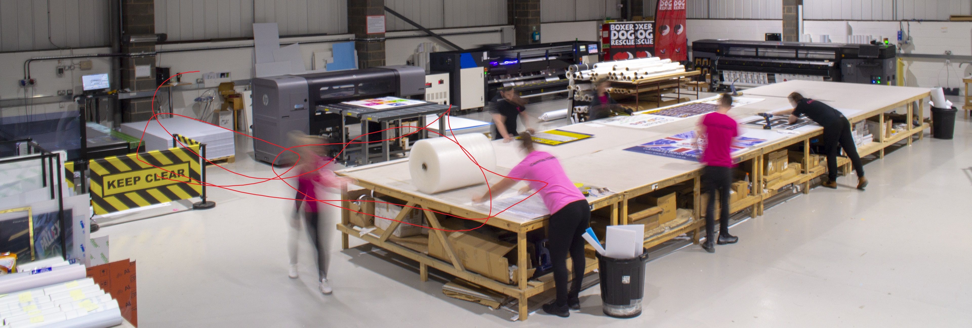 A picture of a large, colourful outdoor hoarding panel featuring a bold, abstract pink design placed at the base of a construction site, advertising the project while providing a creative visual barrier.